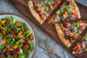 Mehrere Pizzastücke auf einem Holzbrett, daneben alte Gabeln und eine Schüssel mit Salat Mehrere Pizzastücke auf einem Holzbrett, daneben alte Gabeln und eine Schüssel mit Salat